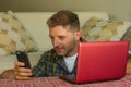 Lifestyle home portrait of young happy and attractive man at home sofa couch working on laptop computer using mobile phone relaxed Royalty Free Stock Photo