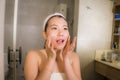 Lifestyle home portrait of young happy and beautiful Asian Japanese woman in bathroom applying facial anti wrinkle cream and serum Royalty Free Stock Photo