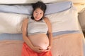 Lifestyle home portrait of young happy and beautiful Asian Korean woman pregnant lying on bed relaxed and excited about maternity Royalty Free Stock Photo