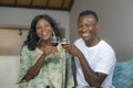 Lifestyle home portrait of young romantic and happy black Afro American couple in love drinking wine cup at living room couch