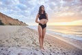 Carefree smiling brunette woman in black swimwear standing on beach, sunny summer day Royalty Free Stock Photo