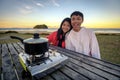 Lifestyle image of young happy asian couple eating hot pot stove on a table outdoor along beach. Leisure activity image of chinese