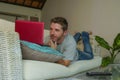 Lifestyle indoors portrait of young attractive and handsome happy man lying at home sofa couch working with laptop computer netboo Royalty Free Stock Photo