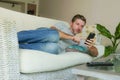 Young handsome attractive happy man using online dating app on mobile phone networking with smartphone lying at home couch Royalty Free Stock Photo