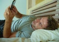 Lifestyle indoors portrait of young happy and attractive man at home bedroom using internet social media app networking from bed s Royalty Free Stock Photo