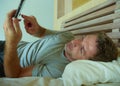 Lifestyle indoors portrait of young happy and attractive man at home bedroom using internet social media app networking from bed s Royalty Free Stock Photo