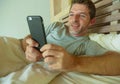 Lifestyle indoors portrait of young happy and attractive man at home bedroom using internet social media app networking from bed s Royalty Free Stock Photo