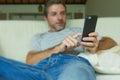 Lifestyle indoors portrait of young happy and attractive man at home sofa couch using internet social media app on mobile phone ne Royalty Free Stock Photo