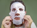 Lifestyle isolated background portrait of young weird and funny man at home trying using paper facial mask cleansing applying anti