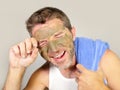 Young attractive and happy man with bathroom towel laughing of himself in the mirror with green cream on his face applying facial Royalty Free Stock Photo