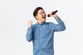 Lifestyle, leisure and people concept. Carefree happy asian man enjoying singing at karaoke, holding microphone and fist Royalty Free Stock Photo