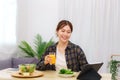 Lifestyle in living room concept, Young Asian woman touching on tablet and drinking orange juice Royalty Free Stock Photo
