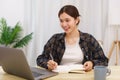 Lifestyle in living room concept, Young Asian woman using laptop and taking notes data on notebook Royalty Free Stock Photo