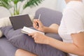 Lifestyle in living room concept, Young Asian woman writing data on notebook while sitting on couch Royalty Free Stock Photo