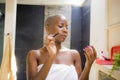 Lifestyle natural portrait of young attractive and happy black african American woman at home bathroom applying face makeup with b