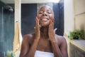 Young attractive and happy black african American woman at home bathroom looking on toilet mirror applying face beauty moisturizer