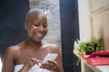 Lifestyle natural portrait of young happy and attractive internet addict afro American woman in home bathroom wrapped in towel usi Royalty Free Stock Photo