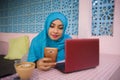 Young beautiful and happy woman in muslim hijab head scarf working with laptop computer and mobile phone networking running inter Royalty Free Stock Photo