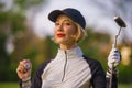 Lifestyle outdoors portrait of young beautiful and happy woman at playing golf holding ball and putter club smiling cheerful in st