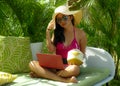 Lifestyle outdoors portrait of young happy and attractive Asian Indonesian teenager girl in bikini and hat working with laptop Royalty Free Stock Photo