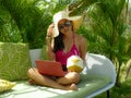 Lifestyle outdoors portrait of young happy and attractive Asian Indonesian teenager girl in bikini and hat working with laptop Royalty Free Stock Photo