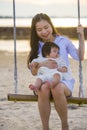 Young sweet and happy Asian Chinese woman holding baby girl swinging together at beach swing on Summer sunset in mother and little Royalty Free Stock Photo