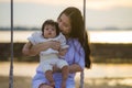 Young sweet and happy Asian Chinese woman holding baby girl swinging together at beach swing on Summer sunset in mother and little Royalty Free Stock Photo