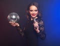 Lifestyle, party and people concept: young woman wearing black dress, holding disco ball and singing into microphone Royalty Free Stock Photo