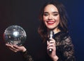 young woman wearing black dress, holding disco ball and singing into microphone over dark background Royalty Free Stock Photo