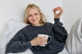 Lifestyle and people concept. Happy blond woman lying in bed with food, drinking tea and eating doughnut, resting at Royalty Free Stock Photo