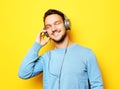 Lifestyle and people concept: young man wearing headphones and holding mobile phone over yellow background Royalty Free Stock Photo