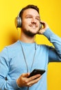 Lifestyle and people concept: young man wearing headphones and holding mobile phone over yellow background Royalty Free Stock Photo