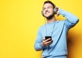 Lifestyle and people concept: young man wearing headphones and holding mobile phone over yellow background Royalty Free Stock Photo