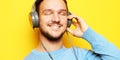 Lifestyle and people concept: young man wearing headphones and holding mobile phone over yellow background. Royalty Free Stock Photo