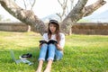 Lifestyle person Girl enjoy listening music and reading a book and play laptop on the grass field of the nature park in the mornin