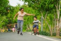 Lifestyle portrait of Asian Indonesian mother and young happy son at city park having fun together the kid learning bike riding Royalty Free Stock Photo