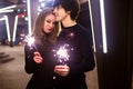 Lifestyle portrait of couple in love holding sparkling New Year fireworks on the city streets with lot of lights on background. Royalty Free Stock Photo