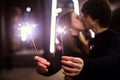 Lifestyle portrait of couple in love holding sparkling New Year fireworks on the city streets with lot of lights on background. Royalty Free Stock Photo