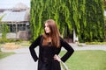 Lifestyle portrait of girl wearing blank black t-shirt, jeans and coat posing against building covered with green leaves Royalty Free Stock Photo