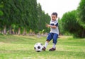 Lifestyle portrait at grass city park of 5 years old Asian Indonesian kid playing football happy and excited kicking the ball