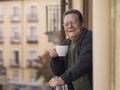Lifestyle portrait of happy and cheerful mature man 65 to 70 years old at home balcony feeling positive and relaxed drinking