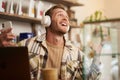 Lifestyle portrait of happy, excited young man, sitting in coffee shop with laptop and headphones, dancing on his chair Royalty Free Stock Photo