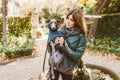 Lifestyle portrait of a happy young female pet lover walking in the park with Italian greyhound breed dog. Puppy is wearing