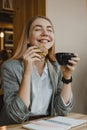 Lifestyle Portrait of smiling young casual blonde woman eating a cookie and drinking coffee, tea in cafe. Happy girl eating a diet