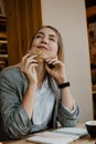 Lifestyle Portrait of smiling young casual blonde woman eating a cookie and drinking coffee, tea in cafe. Happy girl eating a Royalty Free Stock Photo