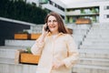 Lifestyle portrait of a stylish young 30s businesswoman talking on cell phone, making call and standing on modern city Royalty Free Stock Photo