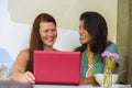 Young happy and beautiful caucasian and hispanic women working at office cafe with laptop computer as digital business partners Royalty Free Stock Photo