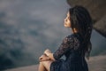 Lifestyle portrait of a woman brunettes in background of lake sitting in sand on a cloudy day. Romantic, gentle, mystical