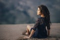 Lifestyle portrait of a woman brunettes in background of lake sitting in sand on a cloudy day. Romantic, gentle, mystical