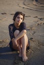 Lifestyle portrait of a woman brunettes in background of lake sitting in sand on a cloudy day. Romantic, gentle, mystical